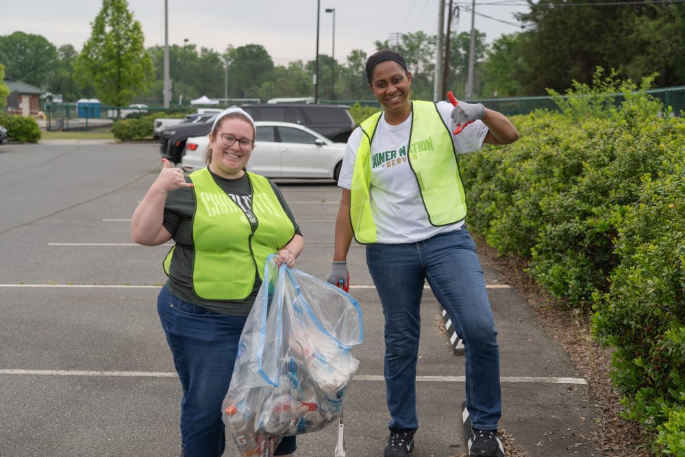 Two UNC Charlotte staff members hold a bag of trash and do the pickaxe sign